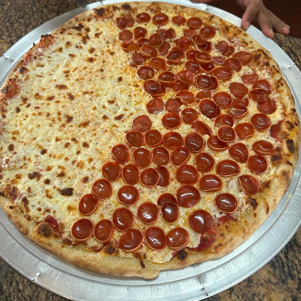 Large half cheese, half pepperoni pizza on a metal tray, with a hand in the background.