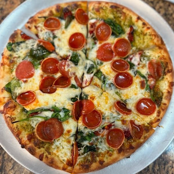 A freshly baked pepperoni pizza with spinach and pesto, sliced and ready to eat.