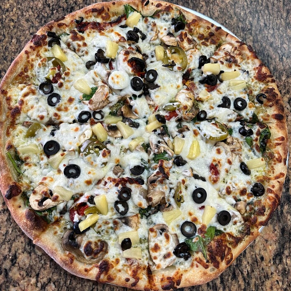 A whole pizza from Slice of Martinez with white sauce, olives, pineapple, mushrooms, and jalapeños.