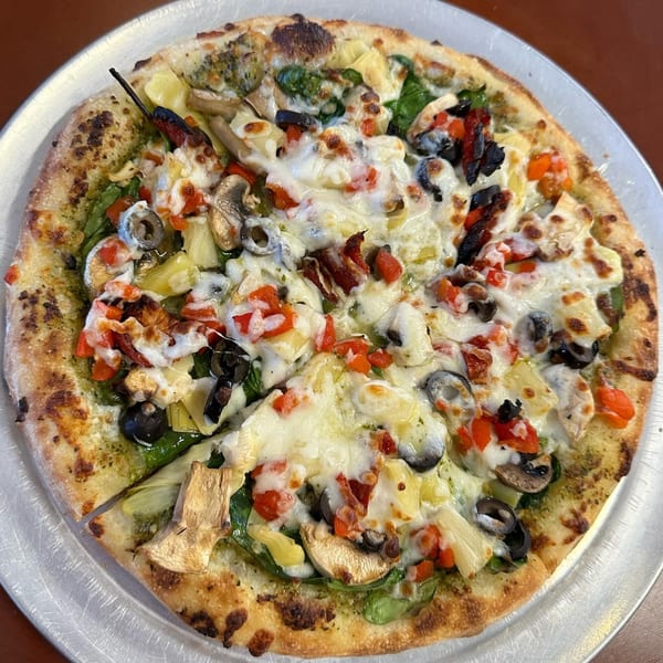 A Slice of Martinez pizza with pesto, mozzarella, spinach, mushrooms, olives, artichoke hearts, and red peppers.