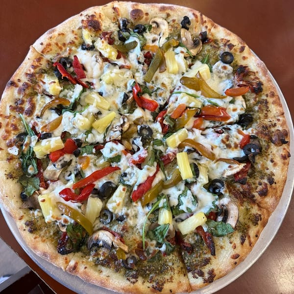 A whole pizza from Slice of Martinez with pesto, cheese, pineapple, olives, mushrooms, and peppers.