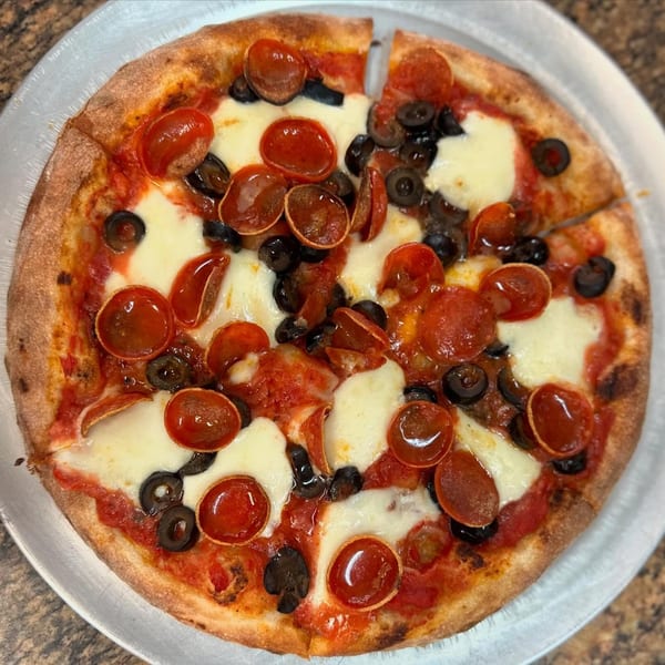 A whole pepperoni and black olive pizza with fresh mozzarella on a metal tray.