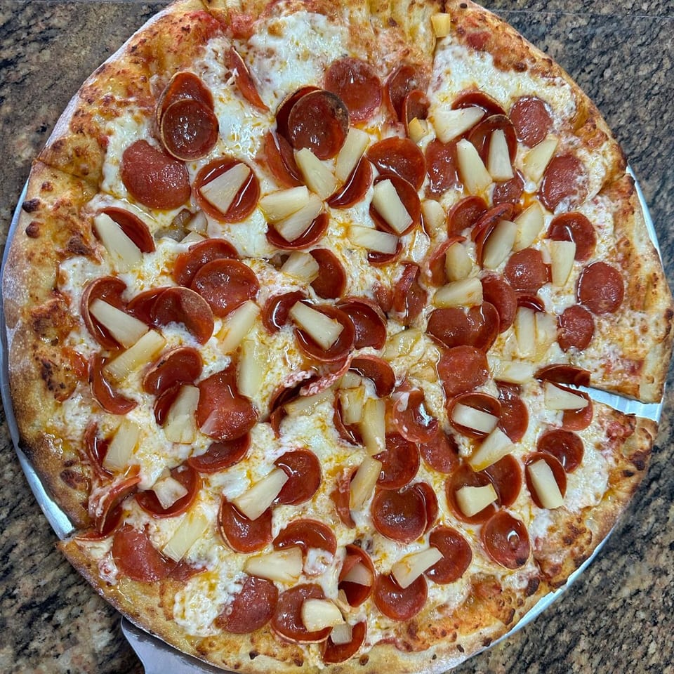 A whole pepperoni and pineapple pizza from Slice of Martinez Pizza and Cheesesteak, with one slice removed.